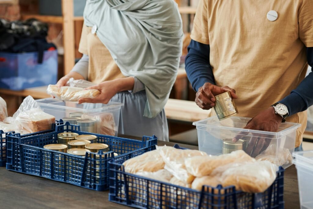 pexels-photo-6995201-6995201 Adults sorting food donations in containers for charity. Community service effort indoors.